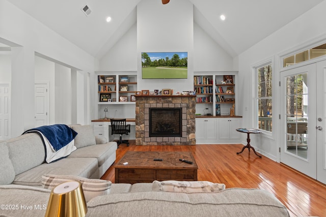 living area featuring french doors, wood-type flooring, visible vents, a stone fireplace, and high vaulted ceiling