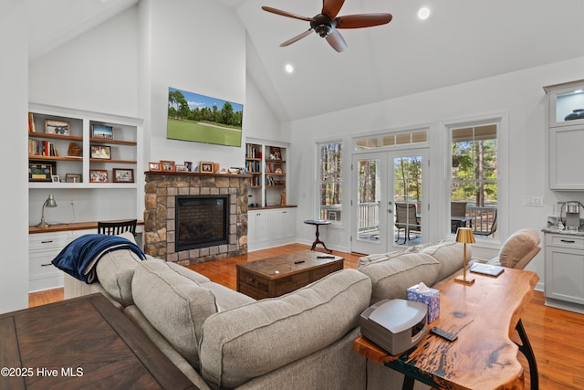 living area with built in shelves, french doors, a fireplace, light wood-style floors, and high vaulted ceiling