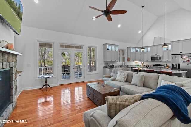 living area with french doors, a fireplace, light wood-style floors, ceiling fan, and high vaulted ceiling