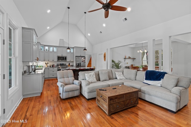 living room with light wood finished floors, visible vents, stairway, high vaulted ceiling, and ceiling fan with notable chandelier