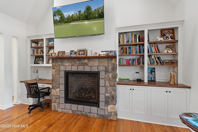 living area featuring built in features, lofted ceiling, a stone fireplace, and light wood finished floors