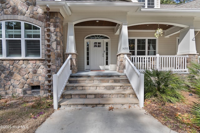 property entrance with stone siding, a porch, crawl space, and roof with shingles