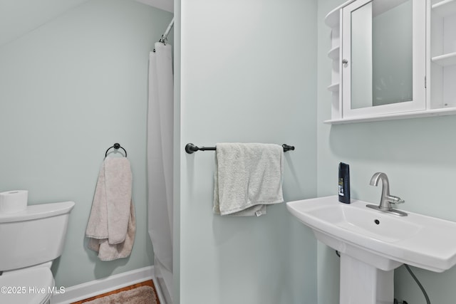 full bathroom featuring toilet, curtained shower, baseboards, and a sink