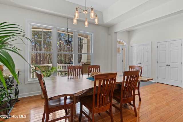 dining area featuring light wood-type flooring, a notable chandelier, and baseboards