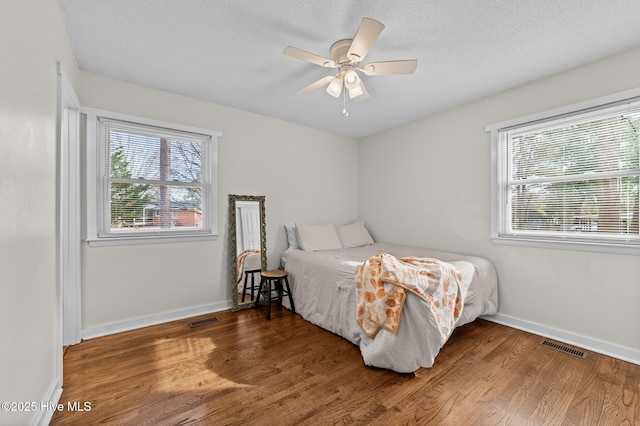 bedroom featuring visible vents, a textured ceiling, baseboards, and wood finished floors