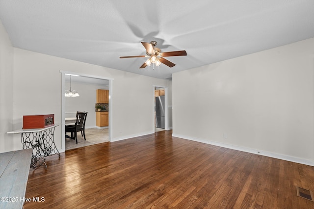 unfurnished living room with ceiling fan with notable chandelier, visible vents, baseboards, and wood finished floors