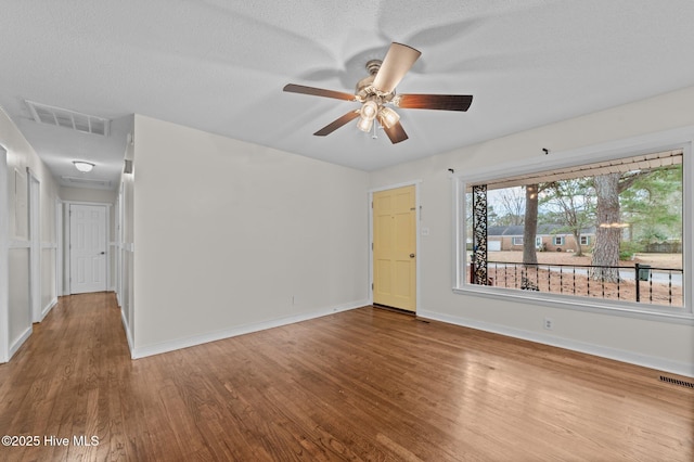 empty room with wood finished floors, visible vents, and baseboards