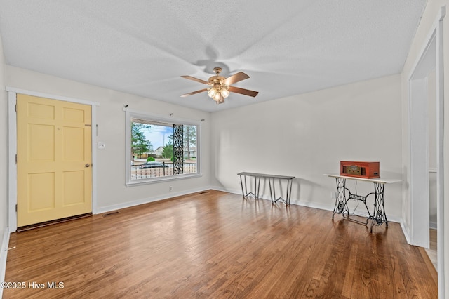 spare room with ceiling fan, a textured ceiling, baseboards, and wood finished floors