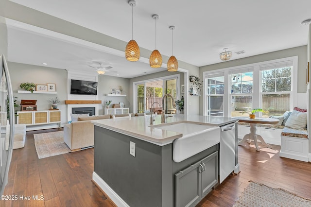 kitchen with a sink, a large fireplace, gray cabinets, stainless steel dishwasher, and dark wood-style flooring