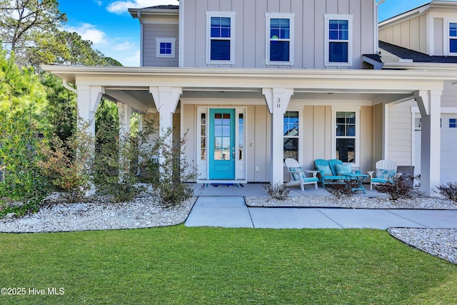 view of exterior entry with covered porch, a lawn, board and batten siding, and outdoor lounge area