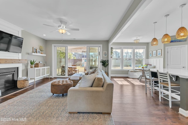 living room with dark wood finished floors, plenty of natural light, a fireplace, and a ceiling fan