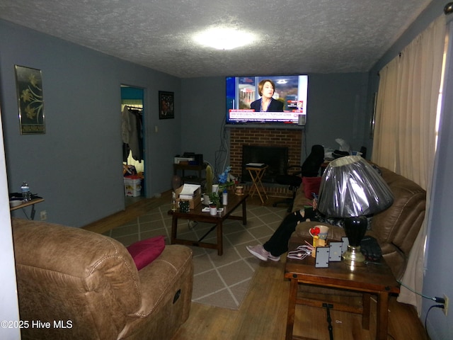 living room with a brick fireplace, a textured ceiling, and wood finished floors