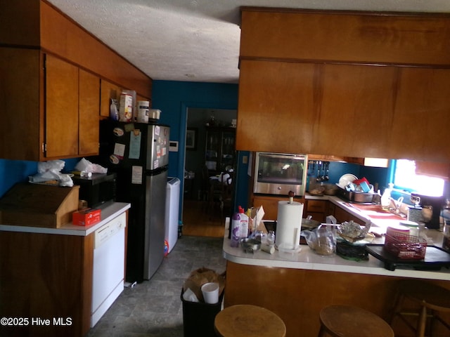 kitchen featuring brown cabinets, a peninsula, stainless steel appliances, light countertops, and a sink