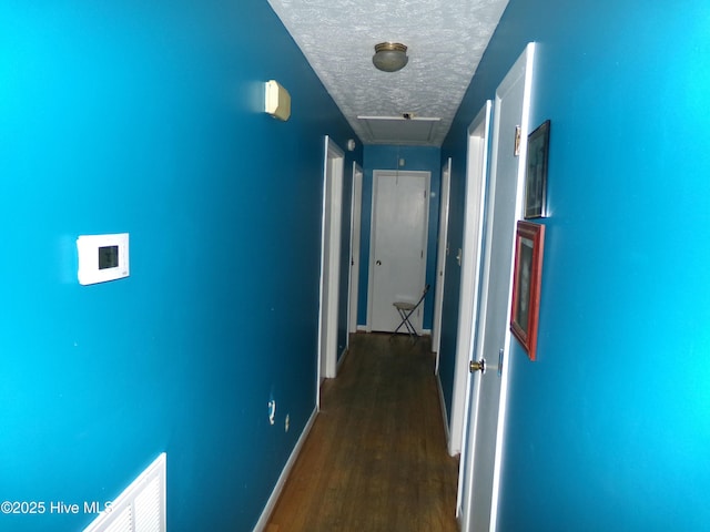 hallway with a textured ceiling, dark wood-type flooring, attic access, and baseboards