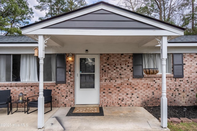 property entrance featuring roof with shingles, a patio, and brick siding