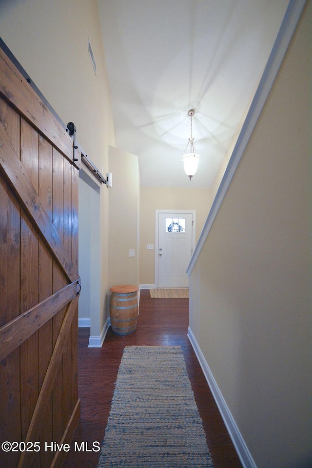 doorway to outside with a barn door, baseboards, visible vents, and dark wood finished floors