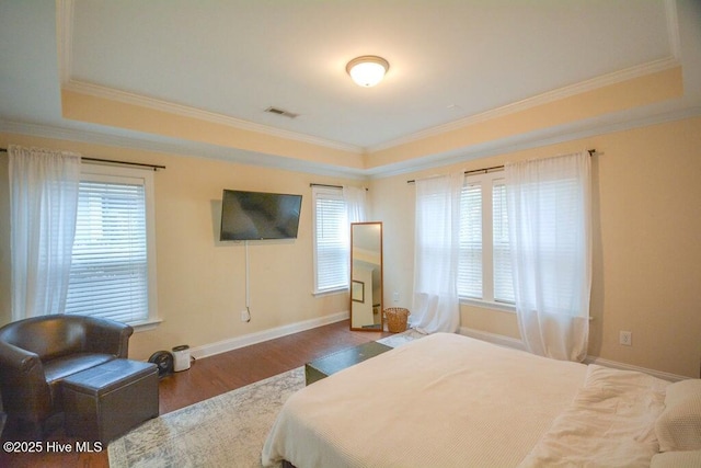 bedroom with visible vents, multiple windows, a tray ceiling, and wood finished floors