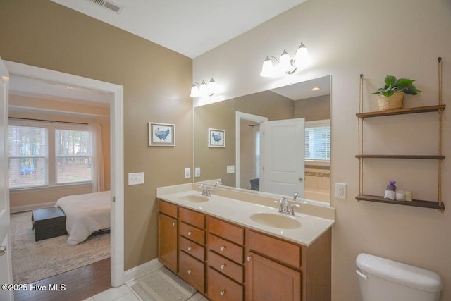 ensuite bathroom with a sink, visible vents, toilet, and double vanity