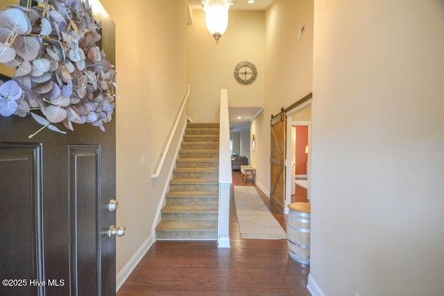 foyer entrance featuring baseboards, stairway, a barn door, a high ceiling, and wood finished floors