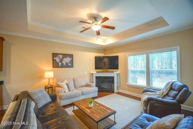 living room featuring a glass covered fireplace, a raised ceiling, wood finished floors, and baseboards