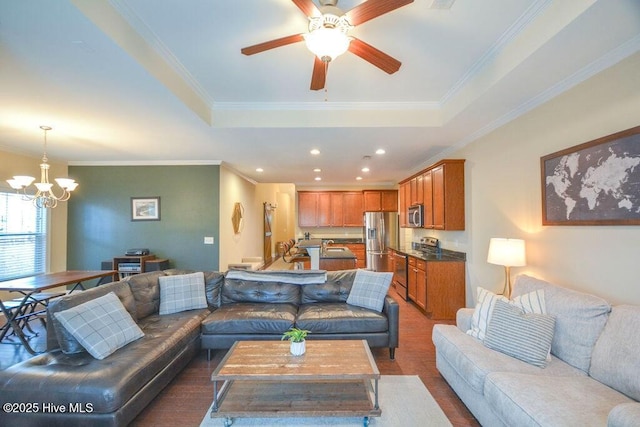 living room featuring ceiling fan with notable chandelier, a raised ceiling, recessed lighting, and crown molding