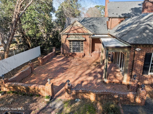 exterior space with a shingled roof, a chimney, fence, and brick siding