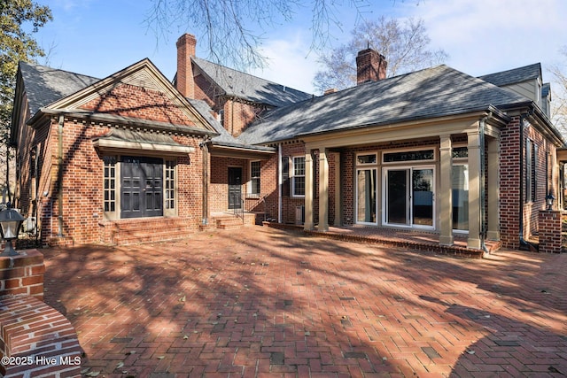 rear view of property with entry steps, roof with shingles, brick siding, and a chimney