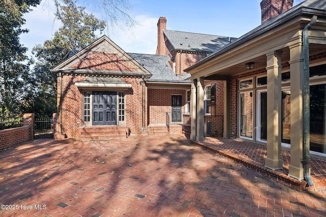 rear view of house featuring a chimney, roof with shingles, fence, a patio area, and brick siding