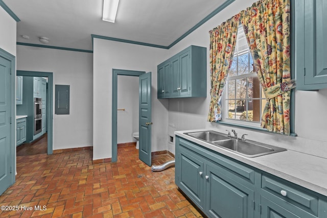 kitchen with brick floor, light countertops, a sink, electric panel, and baseboards