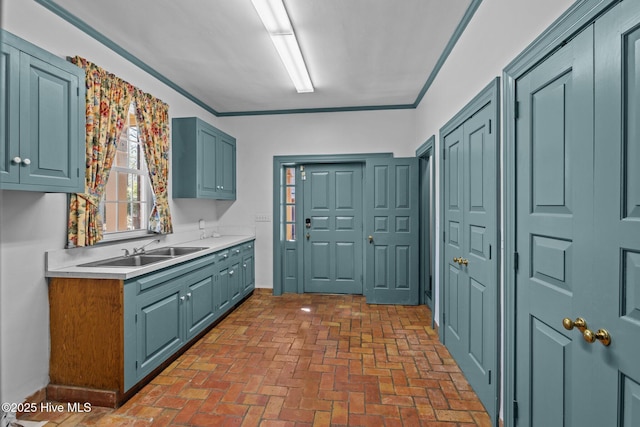 kitchen with blue cabinets, brick floor, light countertops, crown molding, and a sink