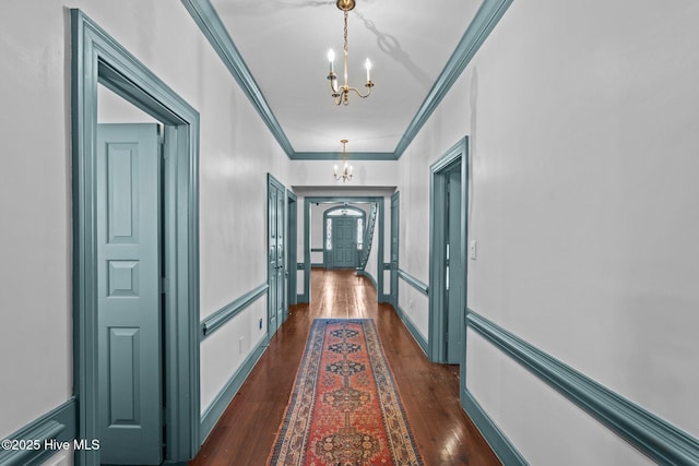 hallway featuring dark wood-style floors, arched walkways, an inviting chandelier, ornamental molding, and baseboards