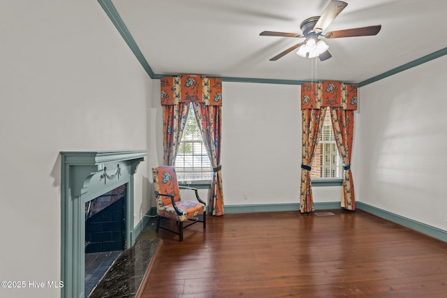 sitting room with hardwood / wood-style floors, a tiled fireplace, ornamental molding, a ceiling fan, and baseboards