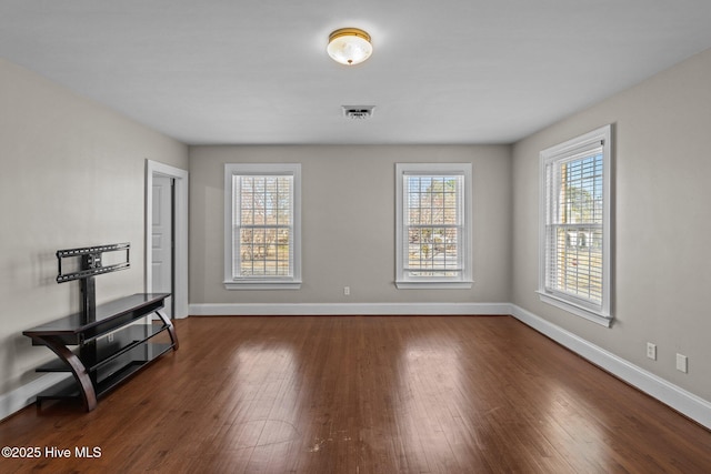 empty room with dark wood-style flooring, visible vents, and baseboards