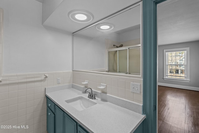 full bathroom with a wainscoted wall, tile walls, a shower with shower door, vanity, and wood finished floors