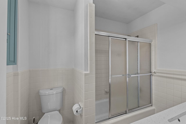 full bath featuring combined bath / shower with glass door, wainscoting, toilet, and tile walls