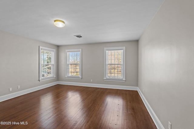 empty room featuring dark wood-type flooring, visible vents, and baseboards