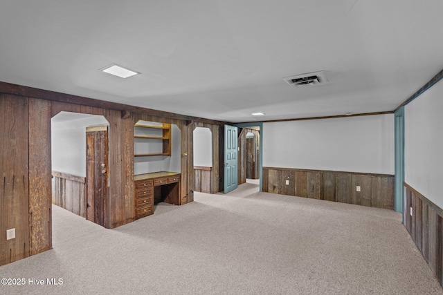 interior space with wood walls, visible vents, built in desk, and a wainscoted wall