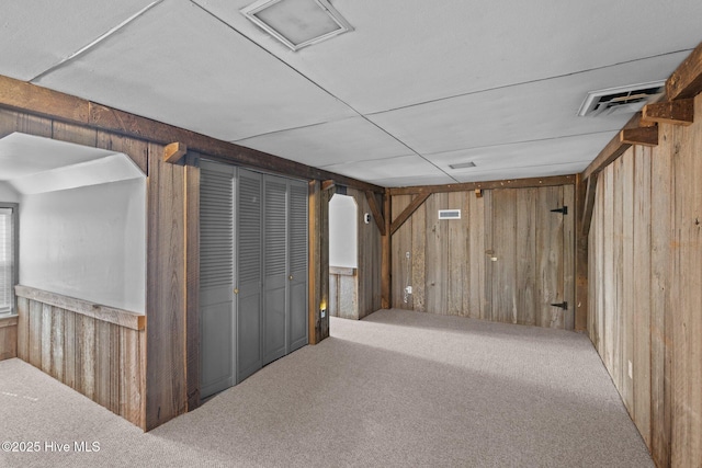 basement with carpet, visible vents, and wood walls