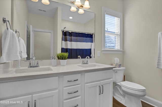 bathroom with toilet, double vanity, a sink, and visible vents