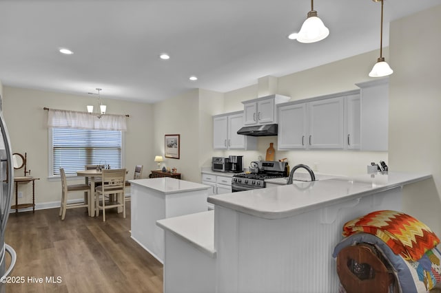 kitchen with a center island, dark wood-style flooring, light countertops, stainless steel range with gas stovetop, and under cabinet range hood