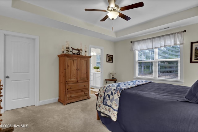 bedroom with a raised ceiling, light colored carpet, visible vents, connected bathroom, and baseboards