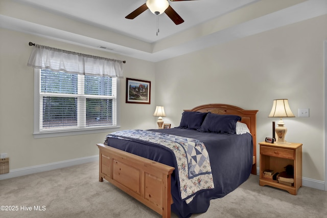 bedroom with ceiling fan, light colored carpet, visible vents, baseboards, and a tray ceiling