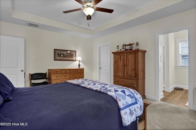 carpeted bedroom with ceiling fan, a raised ceiling, visible vents, and baseboards