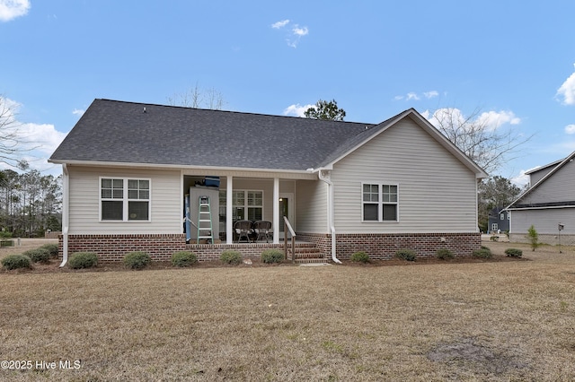 view of front of house with a porch, a front lawn, a shingled roof, and brick siding