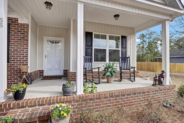 view of exterior entry with covered porch, fence, and brick siding