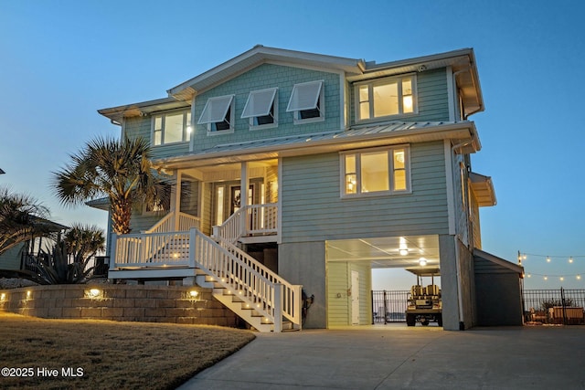 raised beach house featuring stairway, a standing seam roof, covered porch, concrete driveway, and metal roof