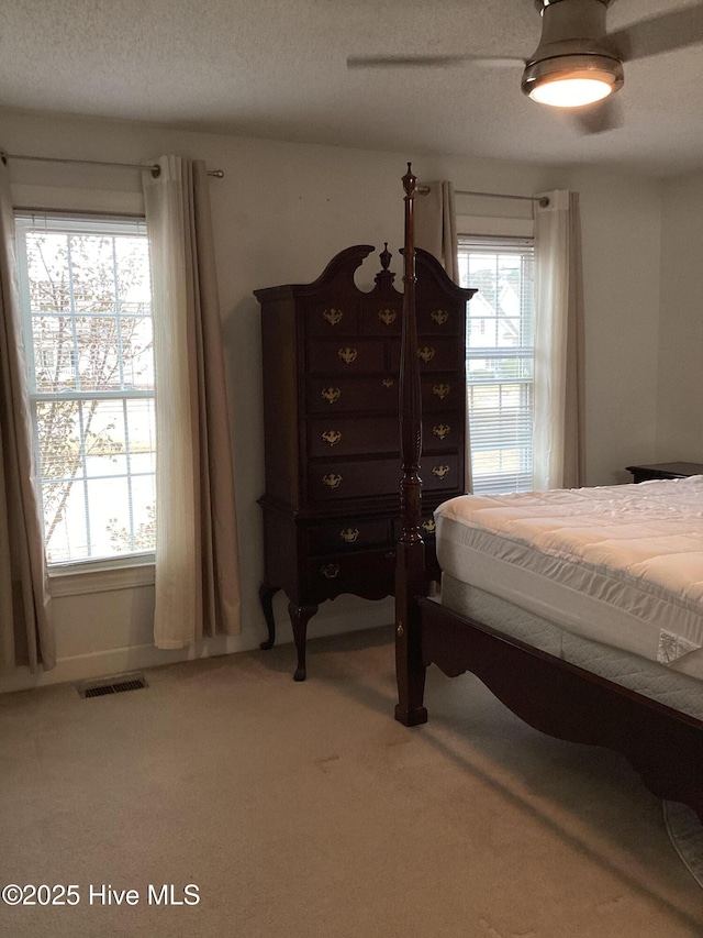 carpeted bedroom featuring visible vents, a textured ceiling, and a ceiling fan