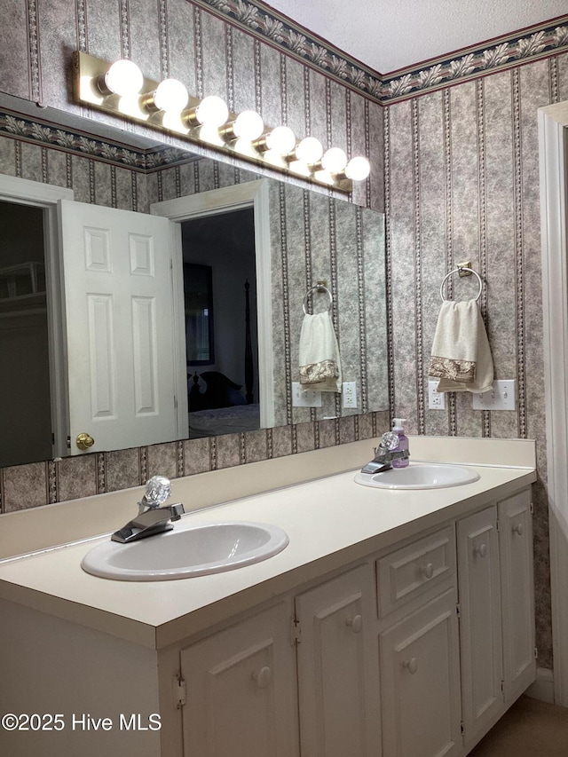 full bathroom with a sink, a textured ceiling, double vanity, and wallpapered walls