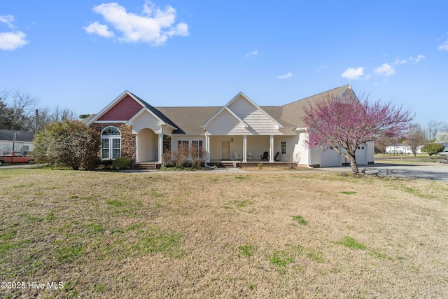 view of front of home with a front yard, covered porch, a garage, stone siding, and driveway