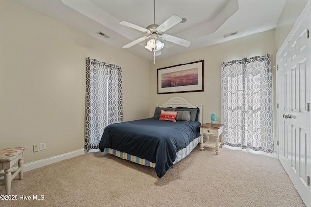 carpeted bedroom featuring a tray ceiling, visible vents, baseboards, and ceiling fan